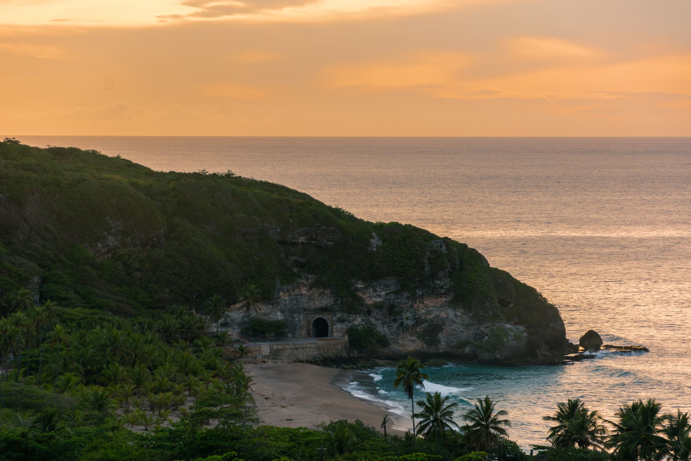 Rugged sea cliffs and rock tunnel along Puerto Rico's northwest Atlantic coast, golden light over the water