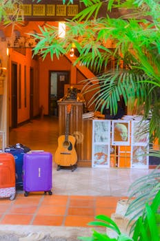 A warm, inviting hostel lobby with tropical decor, luggage, and a guitar.