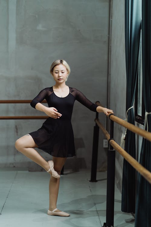 Concentrated young ethnic female dancer doing ballet exercise near barre in studio