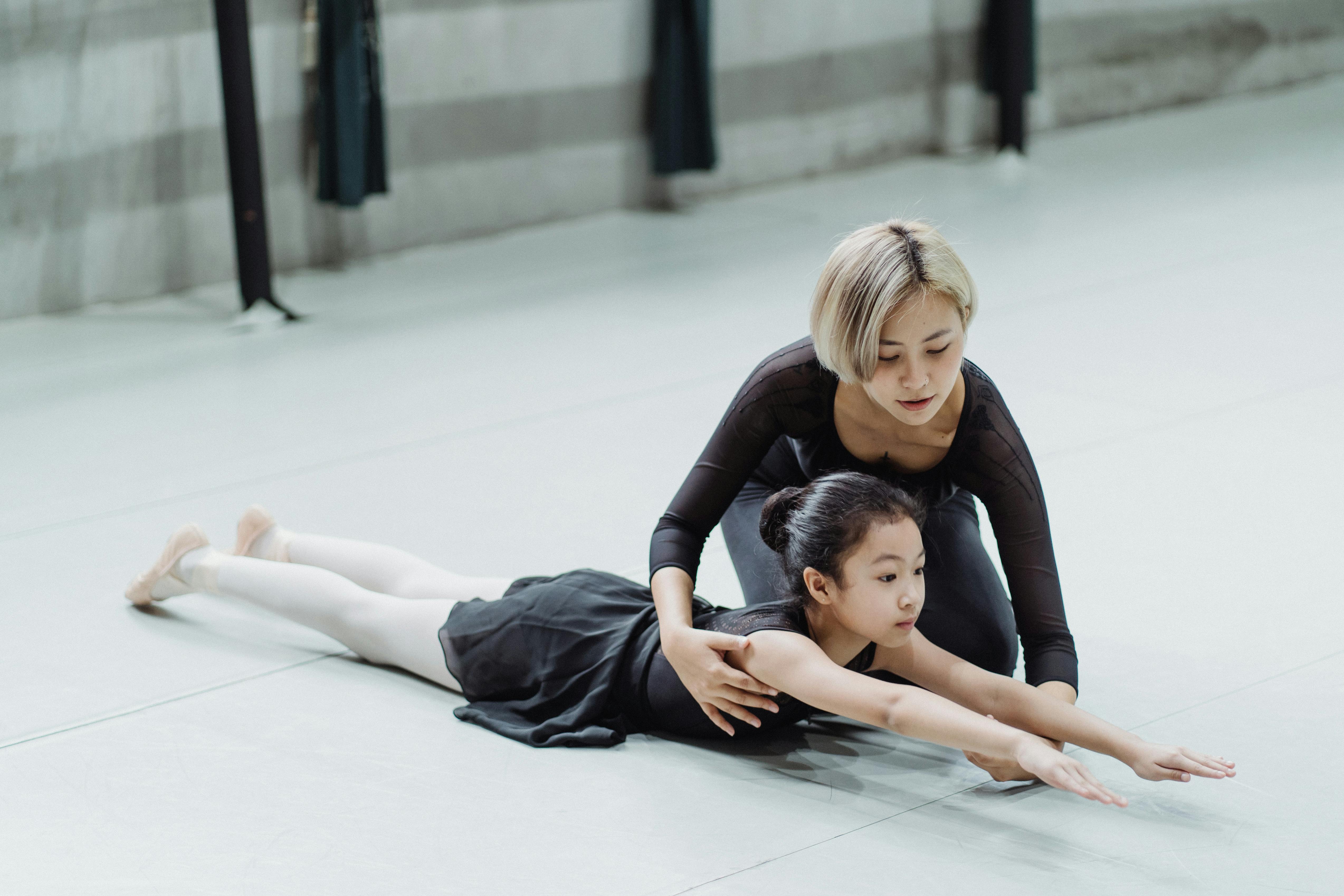 young professional asian ballerina training in studio with adorable little beginner girl