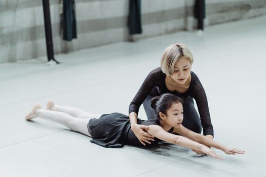 Young professional Asian ballerina training in studio with adorable little beginner girl