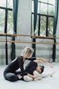 Unrecognizable ballet teacher helping Asian girl to stretch in hall