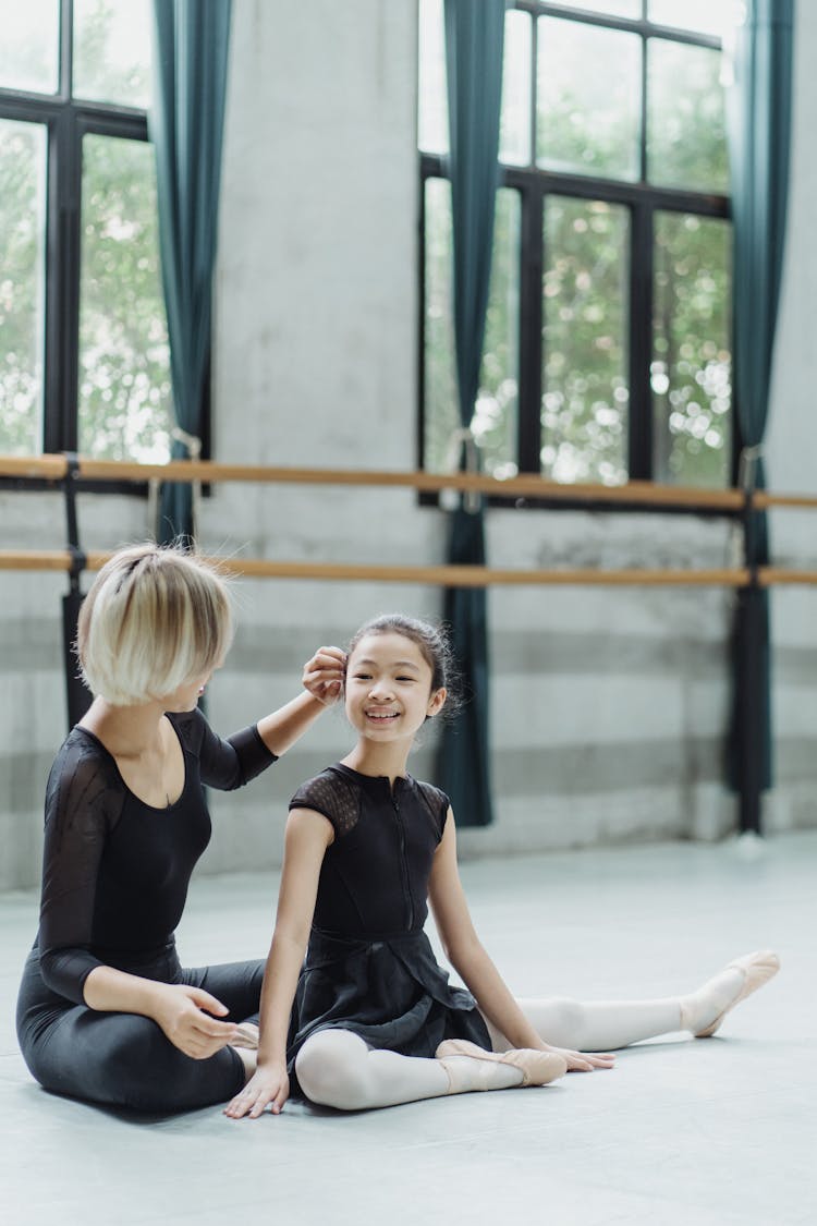 Unrecognizable Trainer Touching Hair Of Asian Girl During Ballet Class