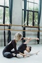 Anonymous instructor helping Asian pupil to stretch during ballet workout