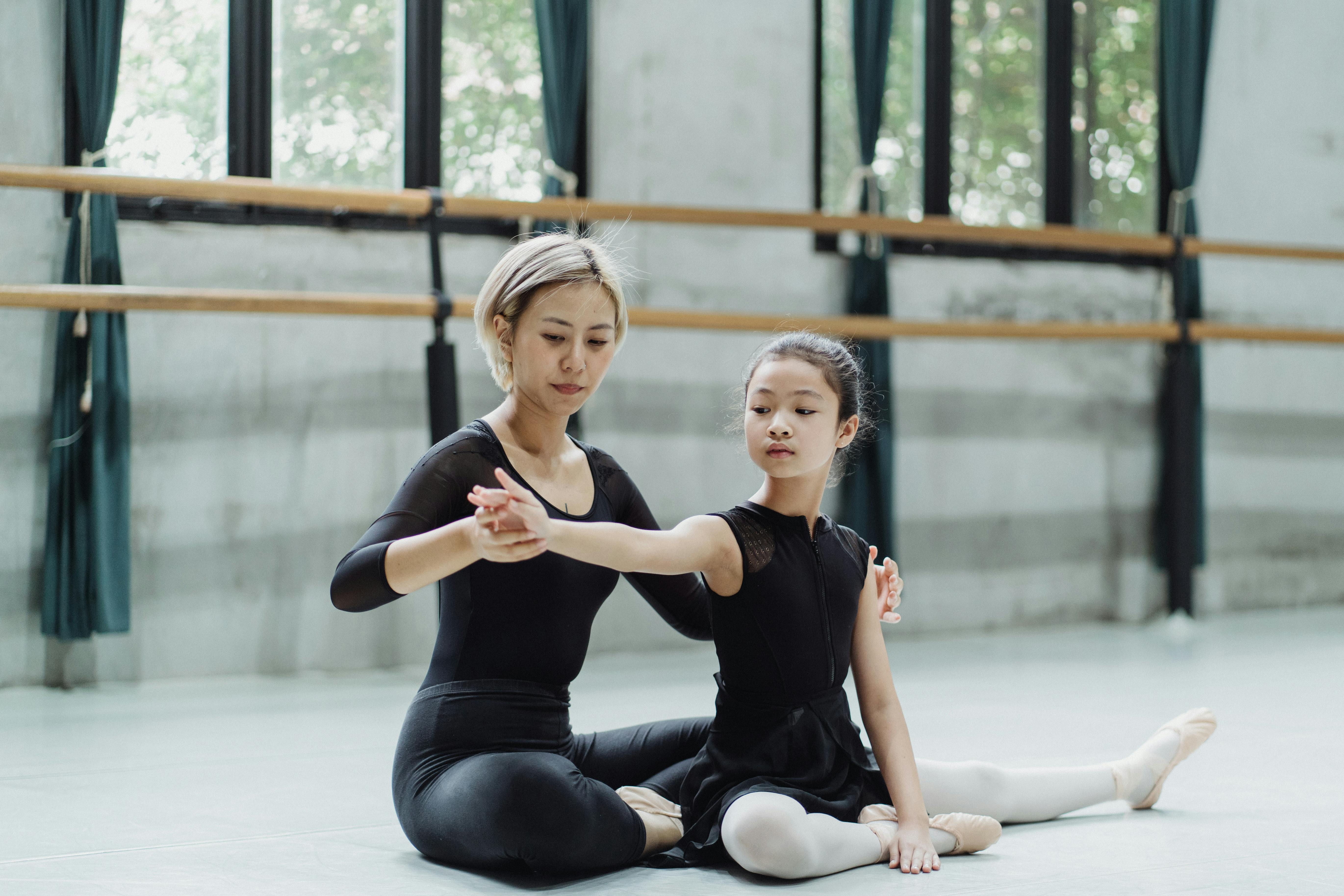 asian female ballerina helping girl during workout on floor