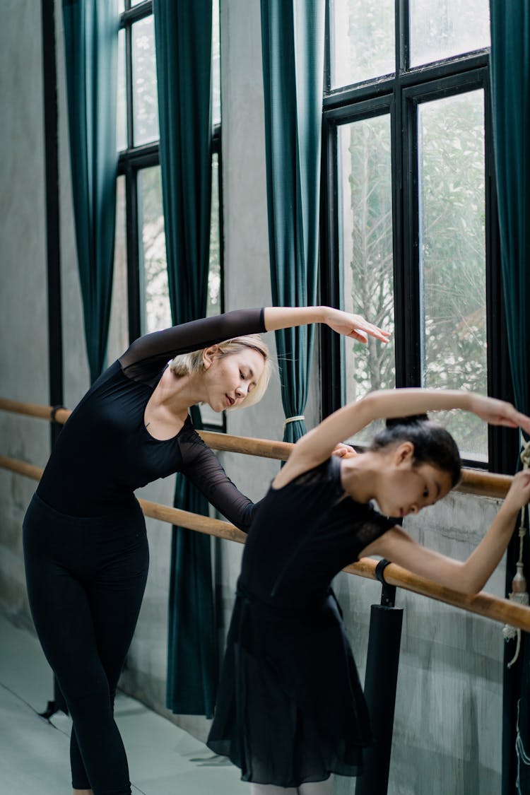 Slim Asian Woman And Girl Ballerinas Bending Gracefully Near Barre