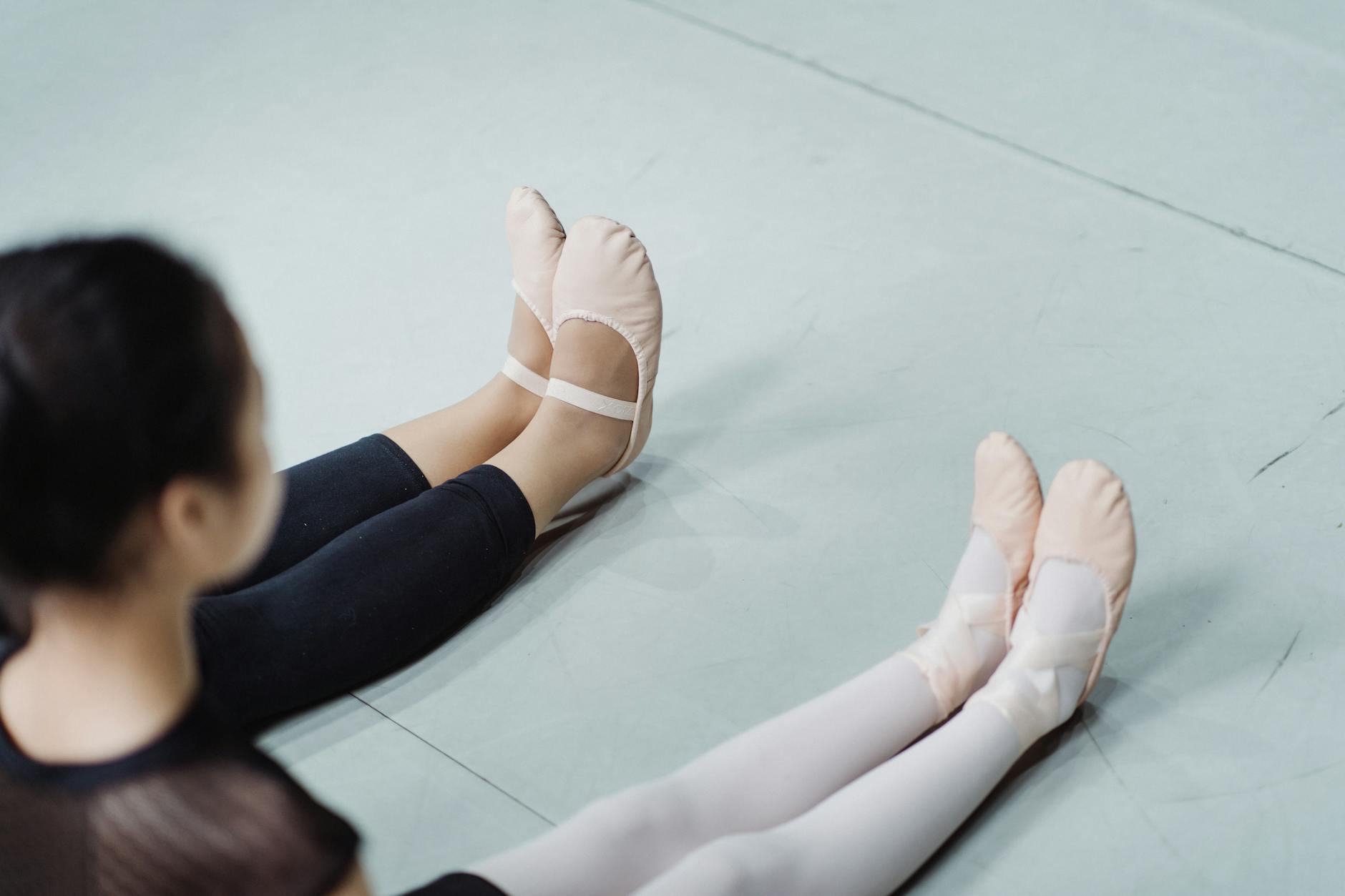 Crop ballerinas in ballet slippers sitting on floor in studio