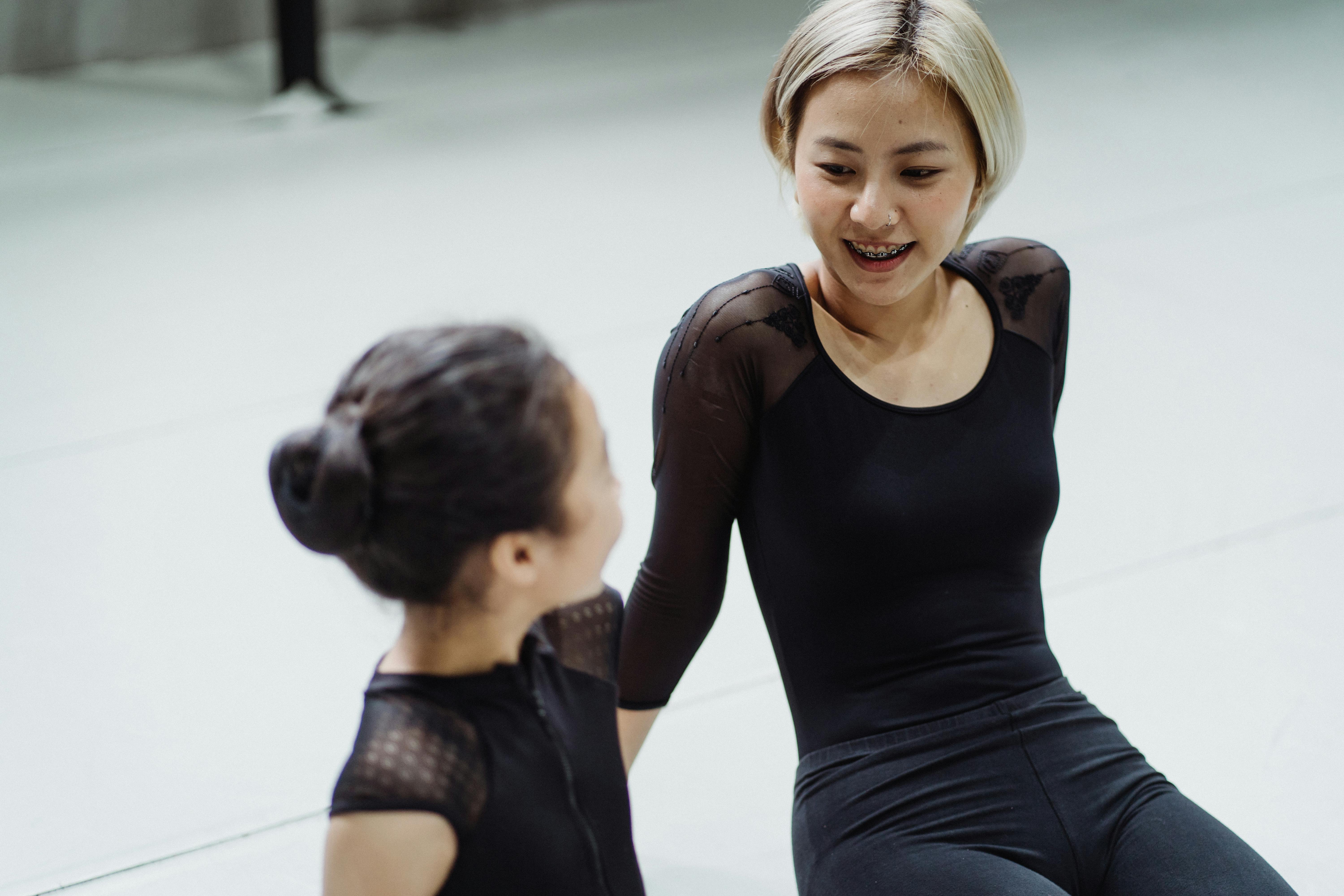 cheerful asian female ballet instructor and trainee sitting on floor