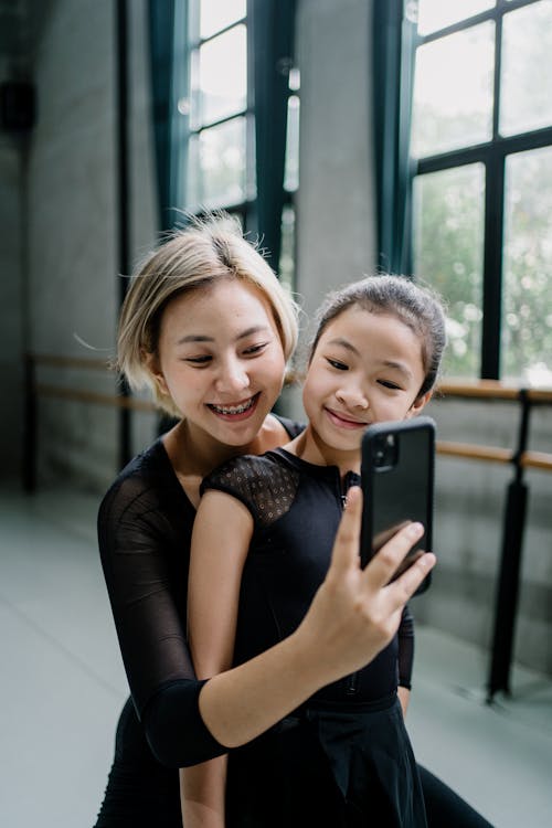 Cheerful Asian ballerinas taking selfie in ballet studio