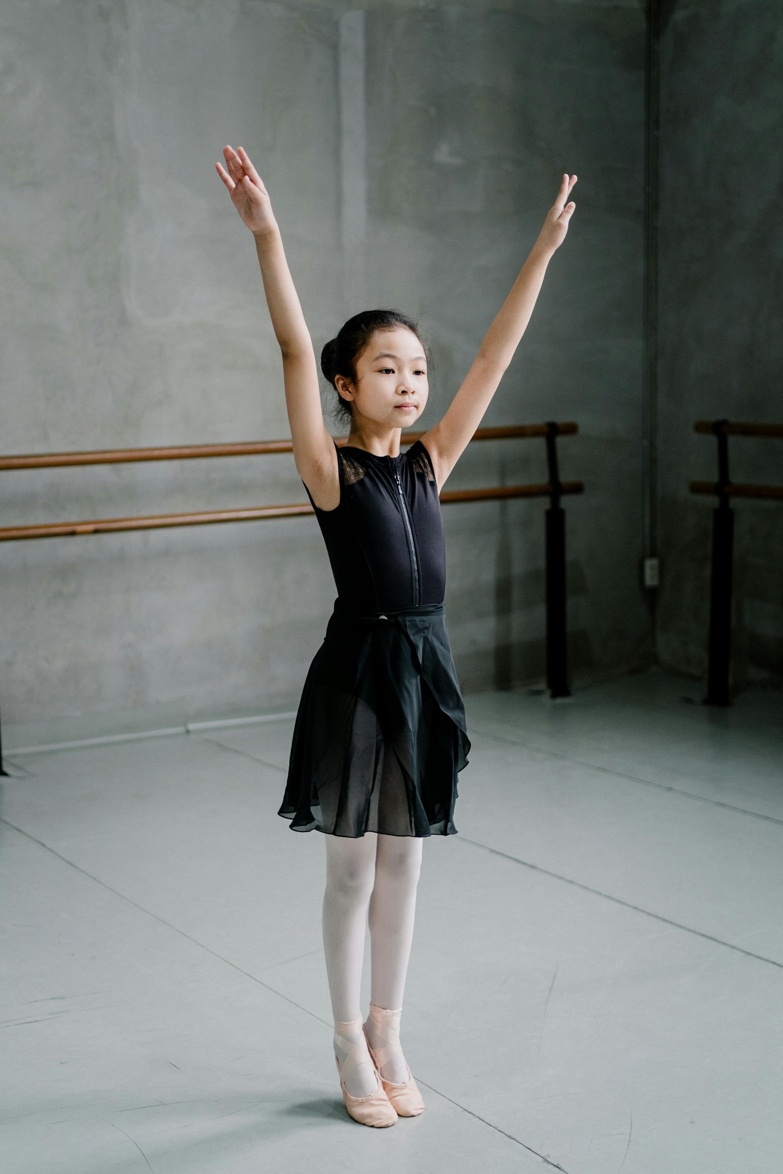 Asian girl ballerina standing with arms raised in studio · Free Stock Photo