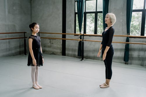 Side view full length Asian female ballerina trainer and girl ballerina standing straight in spacious light ballet studio