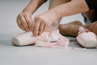Crop faceless ballerina girl tying straps of pointe shoes