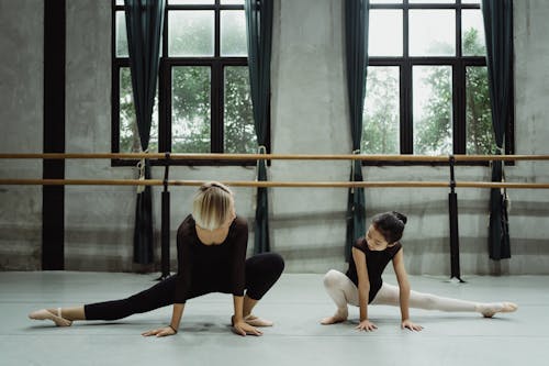 Asian ballerinas stretching legs on floor in spacious studio