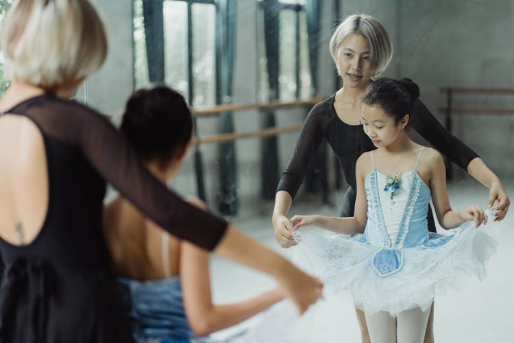 Asian Ballet Instructor And Girl In Tutu Standing Against Mirror