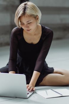 一位积极的亚洲女性身着黑色礼服坐在地板上，手拿字帖，浏览着现代上网本