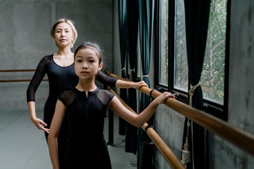 Concentrated ethnic ballerinas practicing ballet with barre in studio