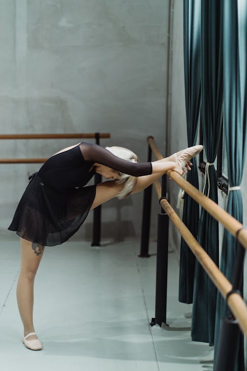 Agile ballerina putting leg on barre and stretching body