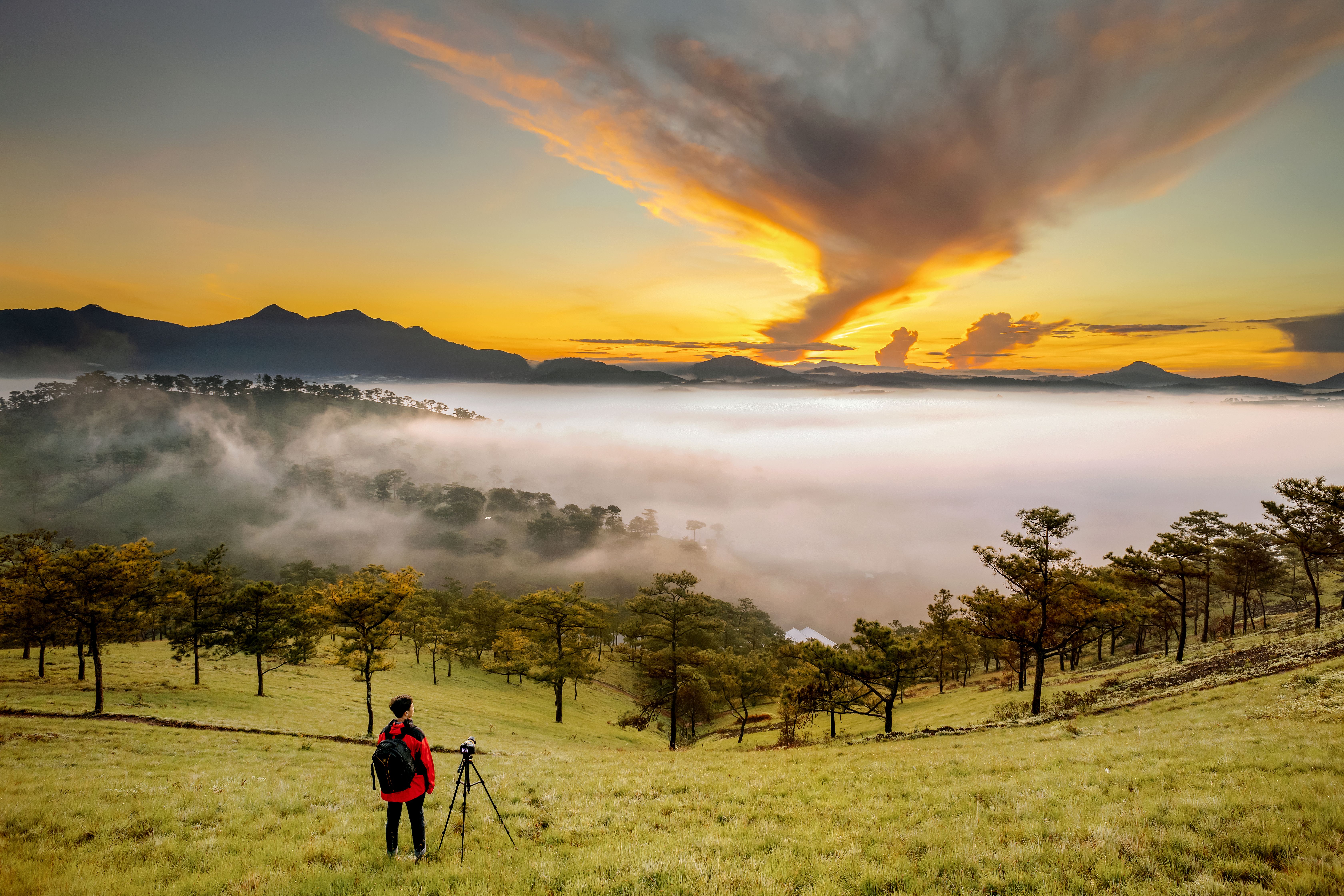 Landscape photographer with tripod standing at sunset in a green mountain valley