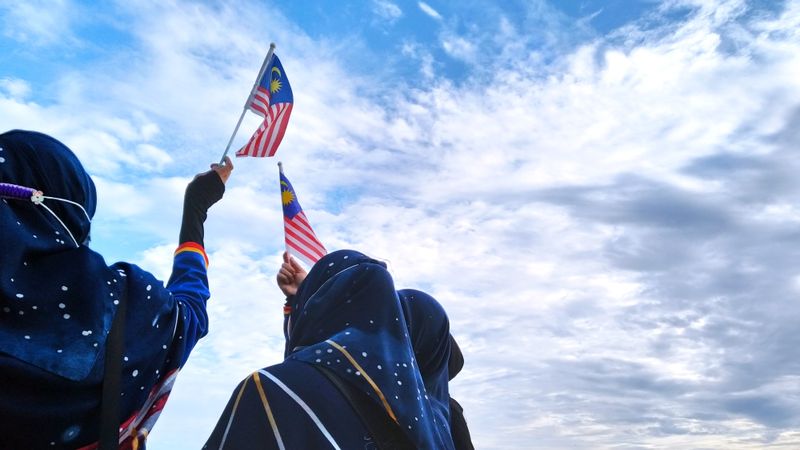 People holding Malaysian flags under a blue sky