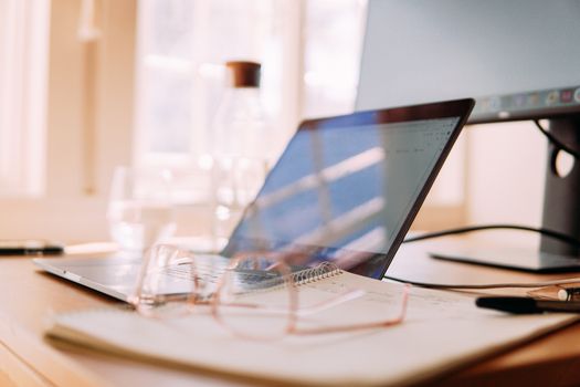 A well-lit home office setup featuring a laptop, monitor, and glasses, ideal for remote work.
