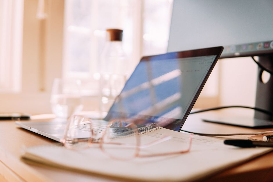 A well-lit home office setup featuring a laptop, monitor, and glasses, ideal for remote work.