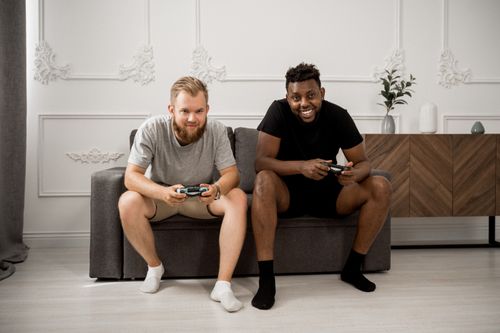 Free Two diverse men happily playing video games together on a stylish sofa indoors. Stock Photo