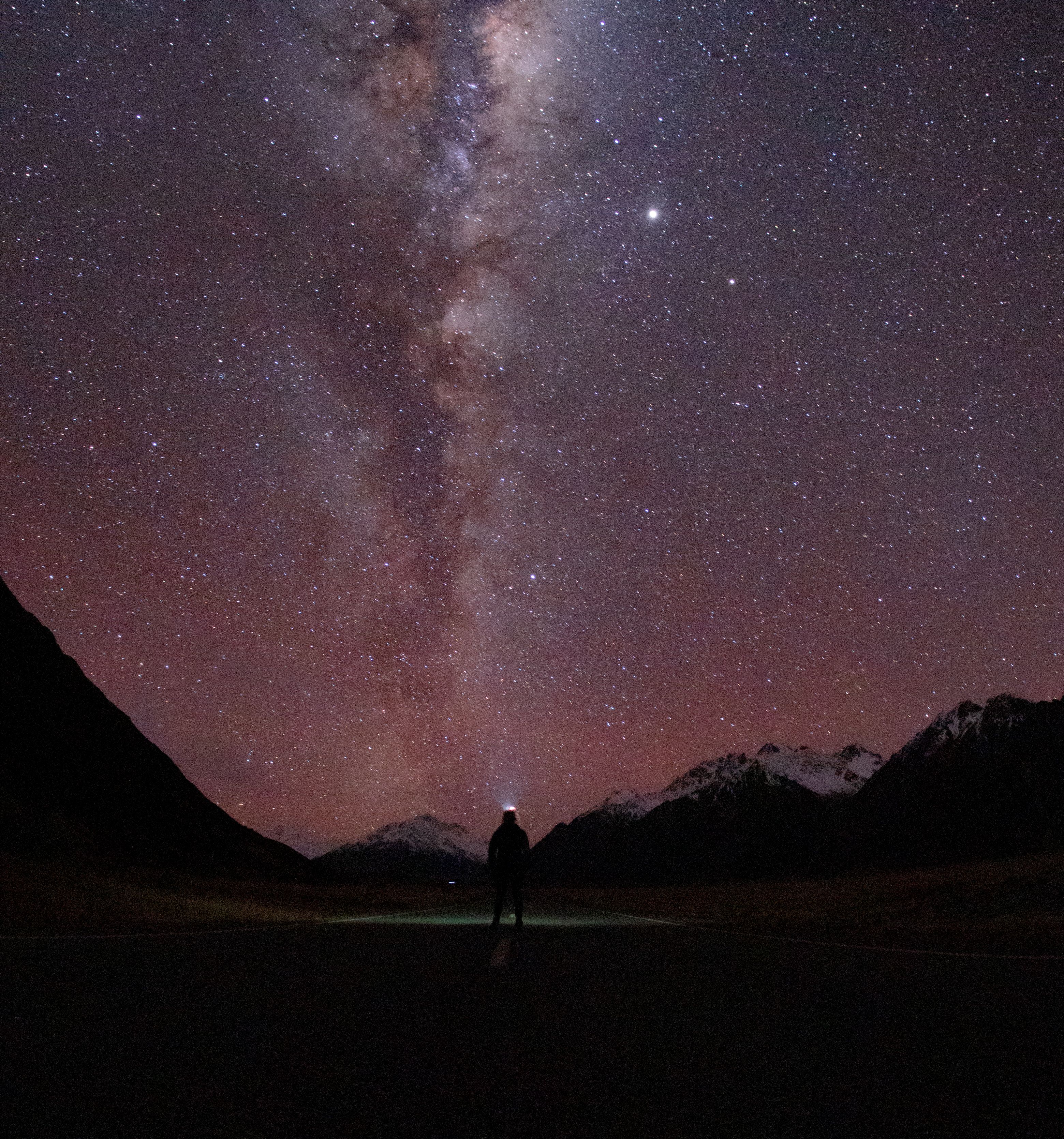 在新西兰坎特伯雷的星空下，一个人站在银河系的映衬下