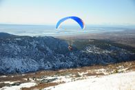 Person in Yellow and Blue Parachute over Gray Rocky Mountain