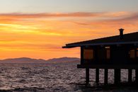 Building on stilts on rippling river near silhouette of rough mountains on picturesque golden sunset