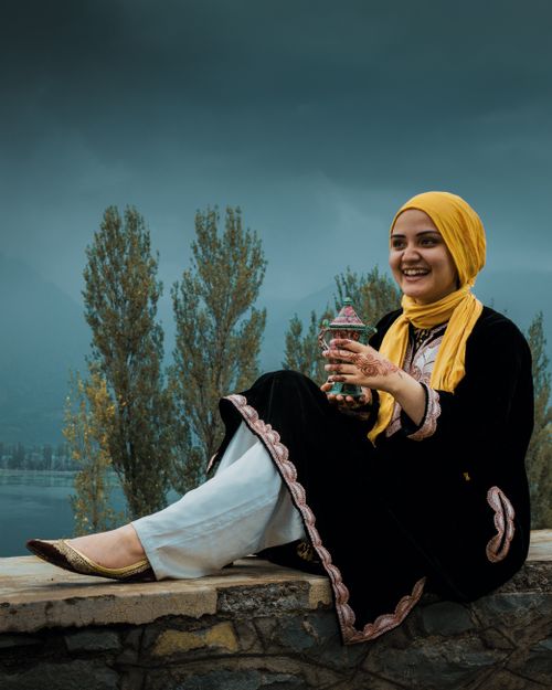 Free A cheerful woman in traditional attire sits outdoors, holding a decorative box, against a scenic background. Stock Photo