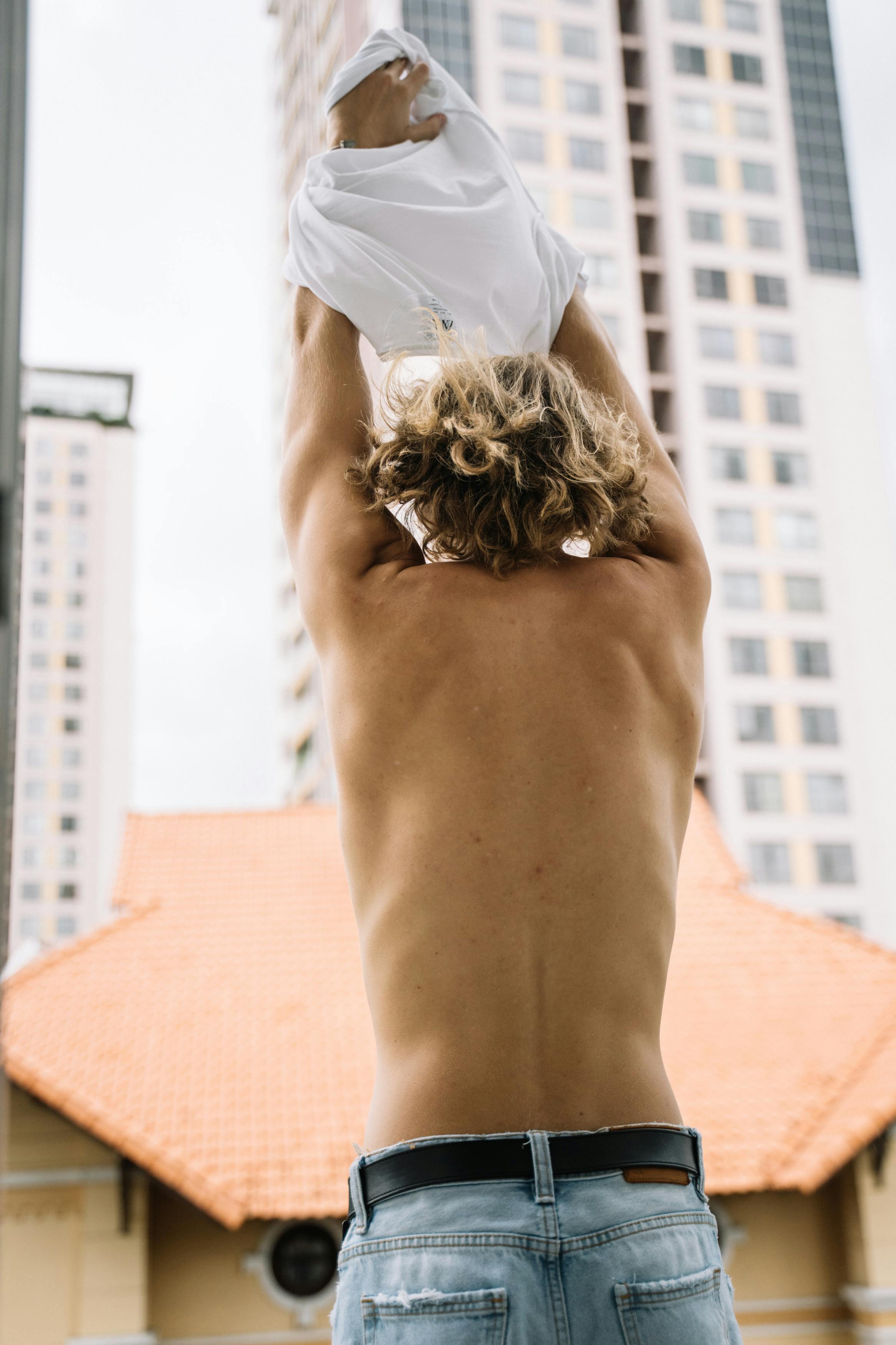 Man with curly hair taking off shirt in an urban setting. Vibrant and modern lifestyle scene.