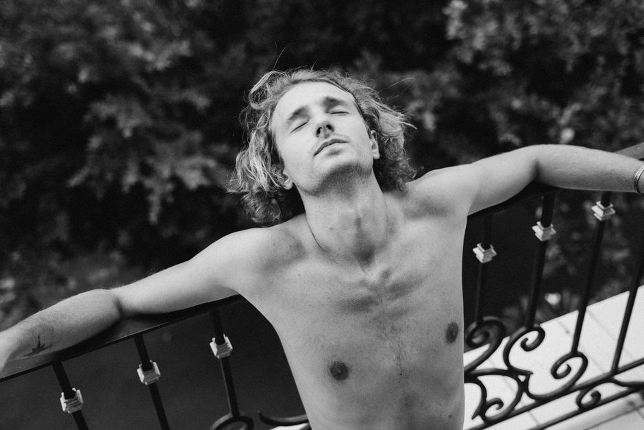 A shirtless man enjoying a serene moment on a balcony, captured in black and white.