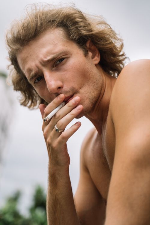 Free Portrait of a shirtless young man smoking a cigarette outdoors with a serious expression. Stock Photo
