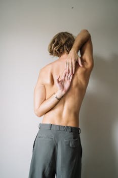 Back view of a shirtless man stretching his arm behind his back.