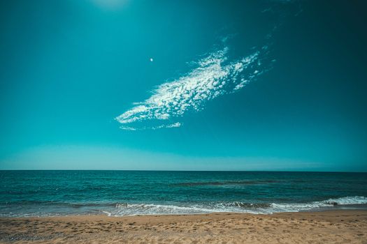 Picturesque scenery of white clouds floating in blue sky over endless sea with foamy waves rolling on sandy beach