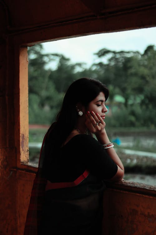 Pensive Indian woman leaning to glassless window in old shabby construction