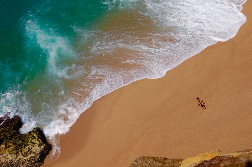 Free Captivating aerial shot of two women walking along a stunning sandy beach with turquoise waves. Stock Photo