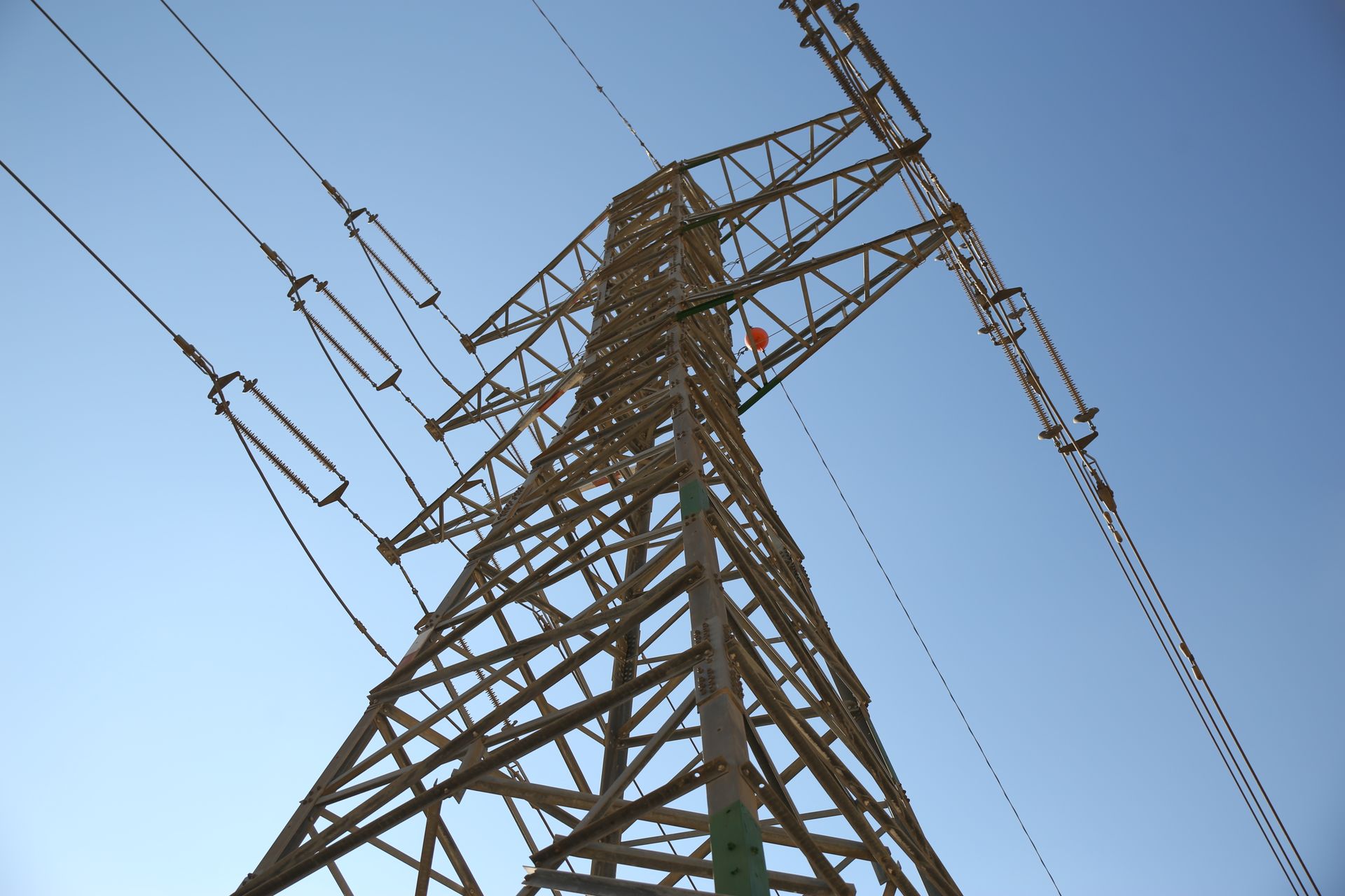 A low-angle view of an electrical transmission tower reaching into a clear blue sky, showcasing its structural details.