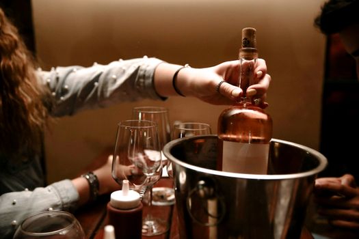 Close-up shot of hands holding a wine bottle at a bar counter with glasses and an ice bucket.