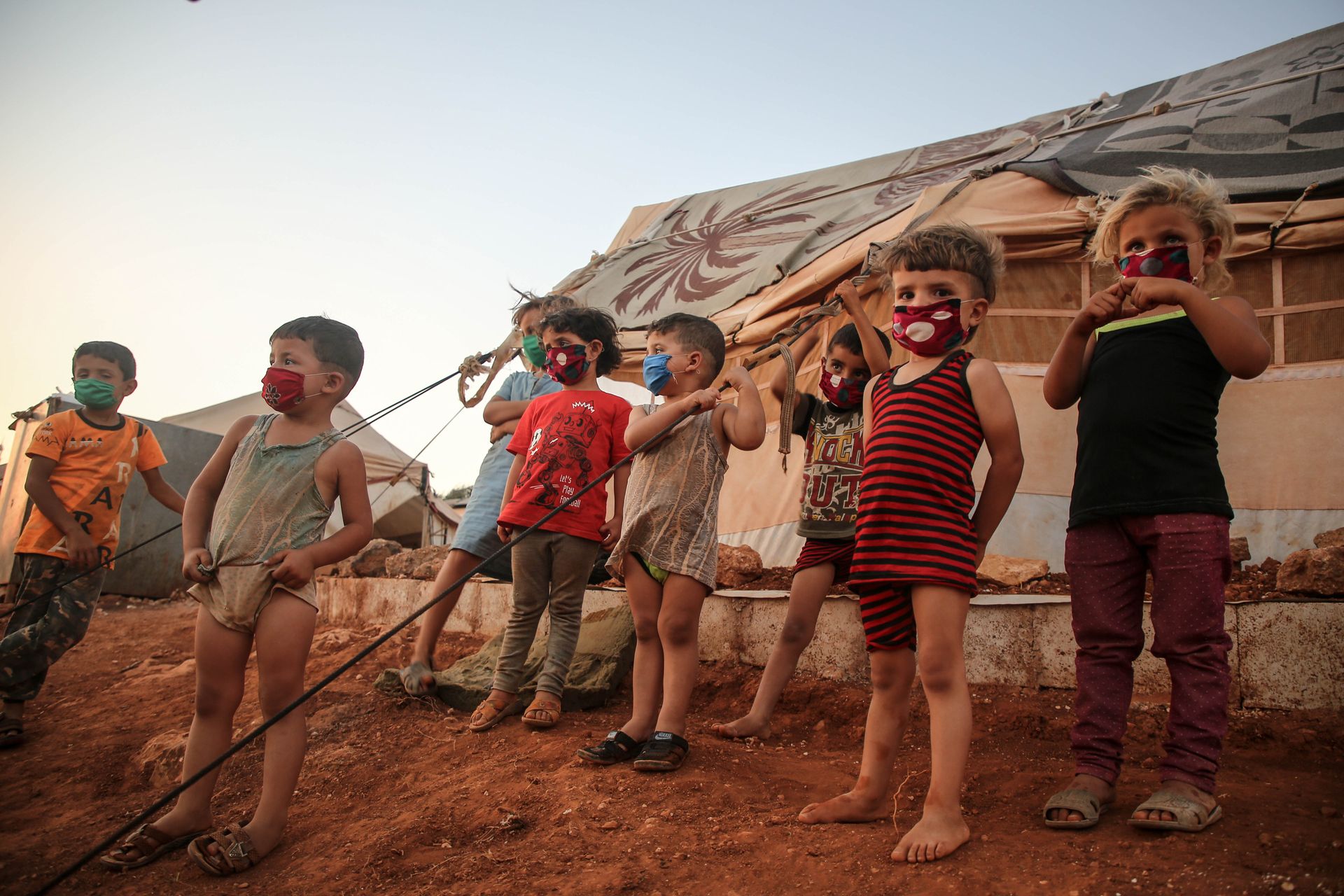 Young children wearing masks in a Syrian refugee camp, highlighting the impact of the pandemic.