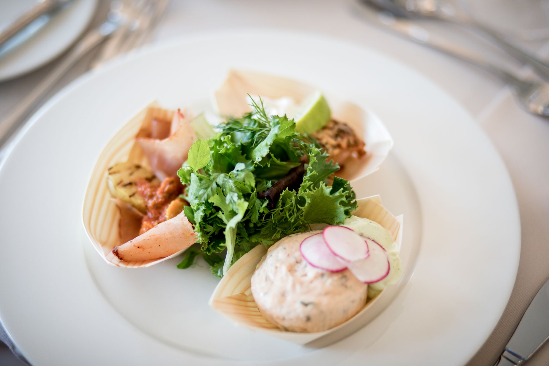 Elegant presentation of gourmet dish with greens, radish, and dips on a plate.