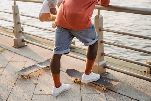 Unrecognizable multiethnic male skater standing near embankment railing with skateboards