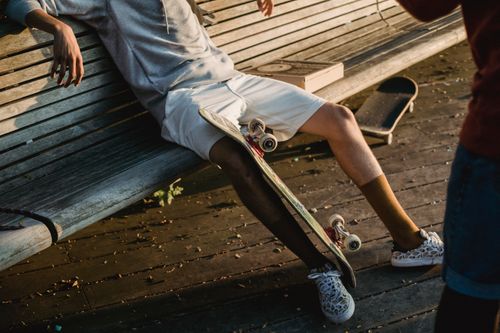 Free Crop unrecognizable male skater in casual summer outfit sitting with skateboard on shabby street bench Stock Photo