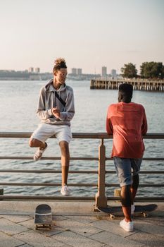 几位穿着休闲服、不同种族的男性溜冰者正站在滨水扶手的滑板旁聊天