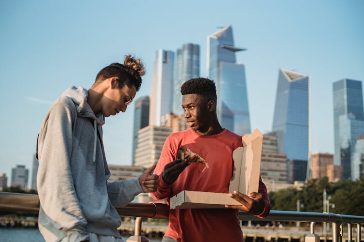 Diverse Male Friend Eating Pizza On Urban City Embankment