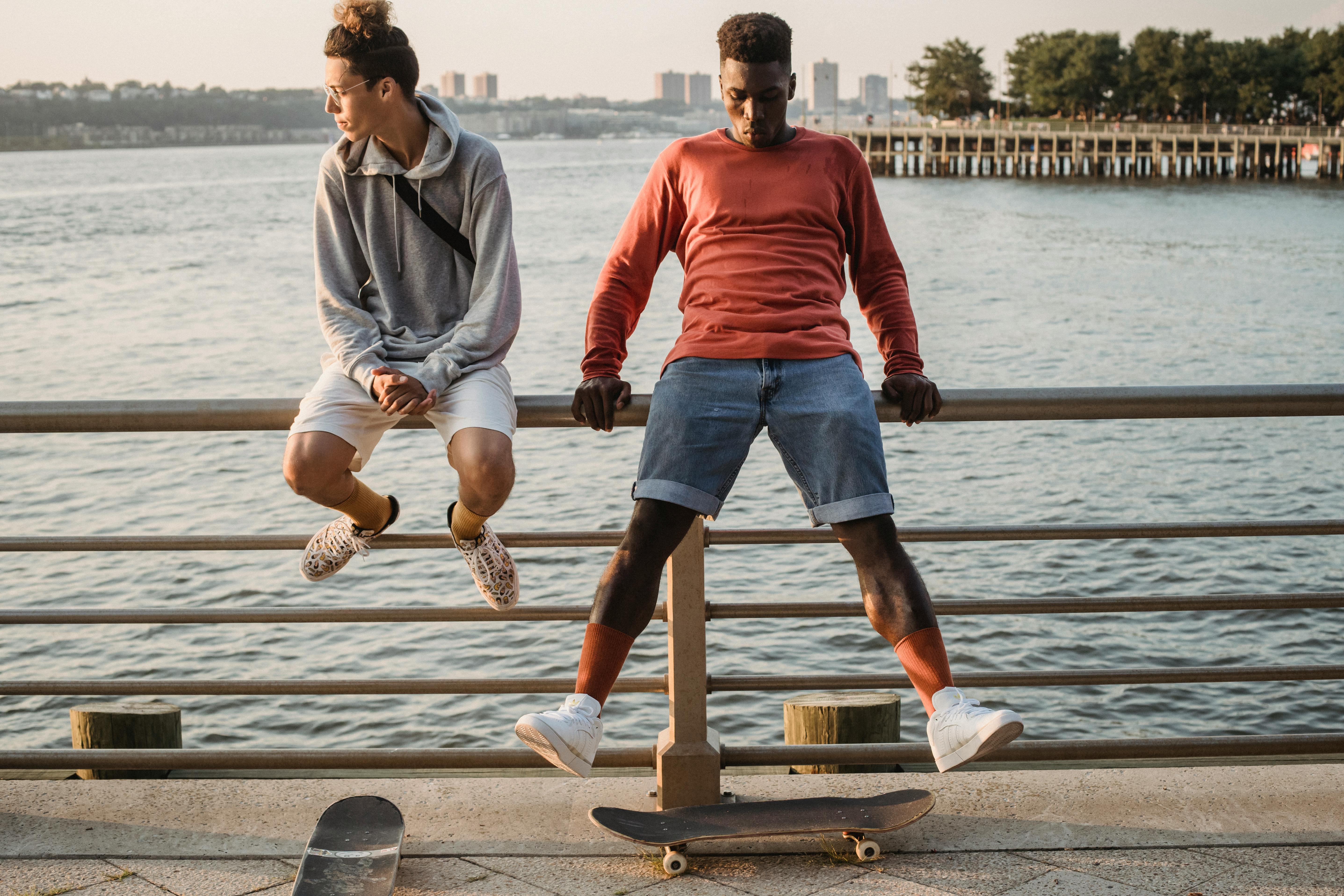 Two young men enjoy skateboarding at a city waterfront during a summer evening.