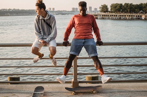 Patineurs Masculins Sportifs Assis Sur La Balustrade De Remblai En Soirée