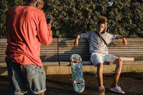 Black man taking photo of male skater sitting on bench