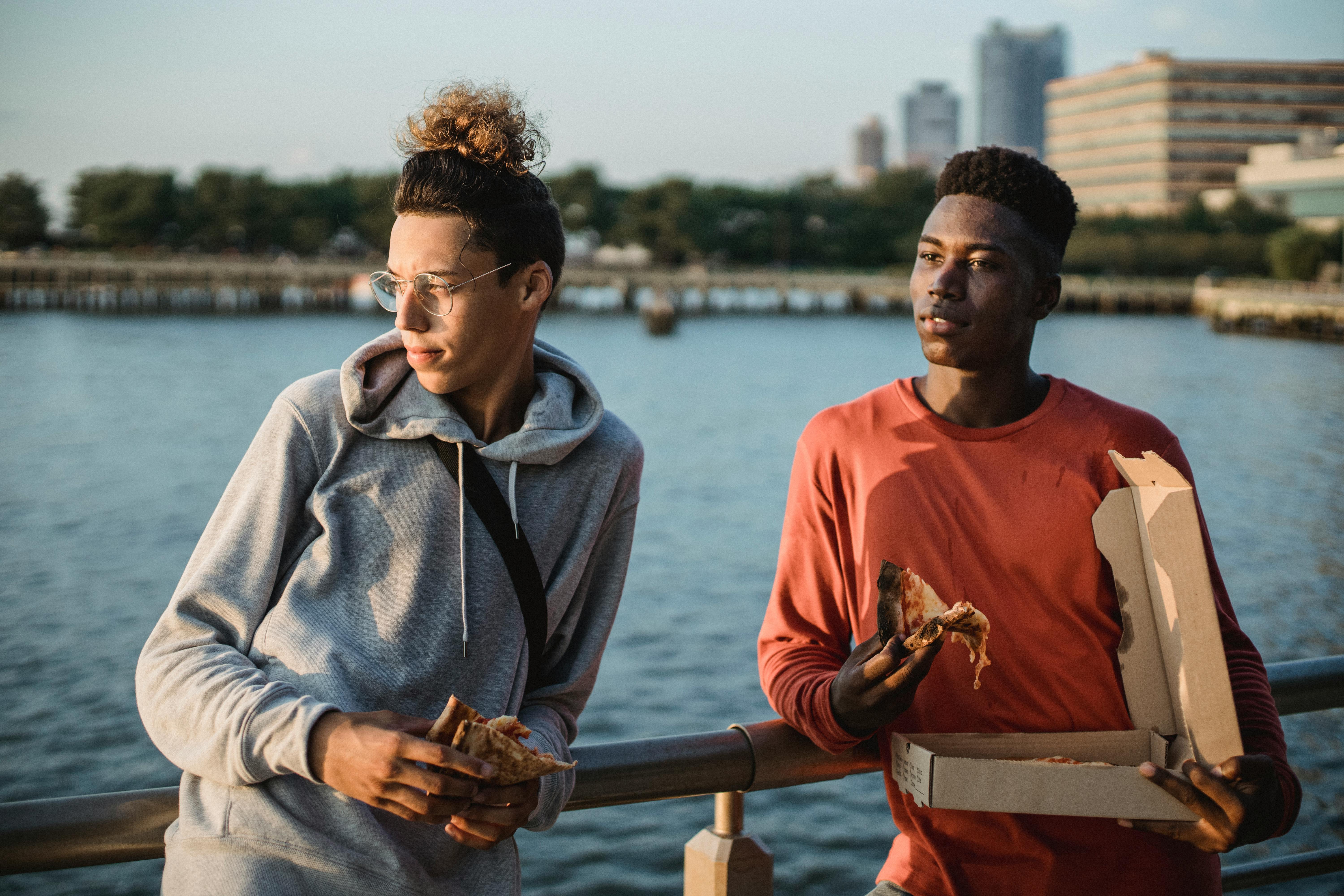 diverse male friends enjoying tasty pizza on city embankment