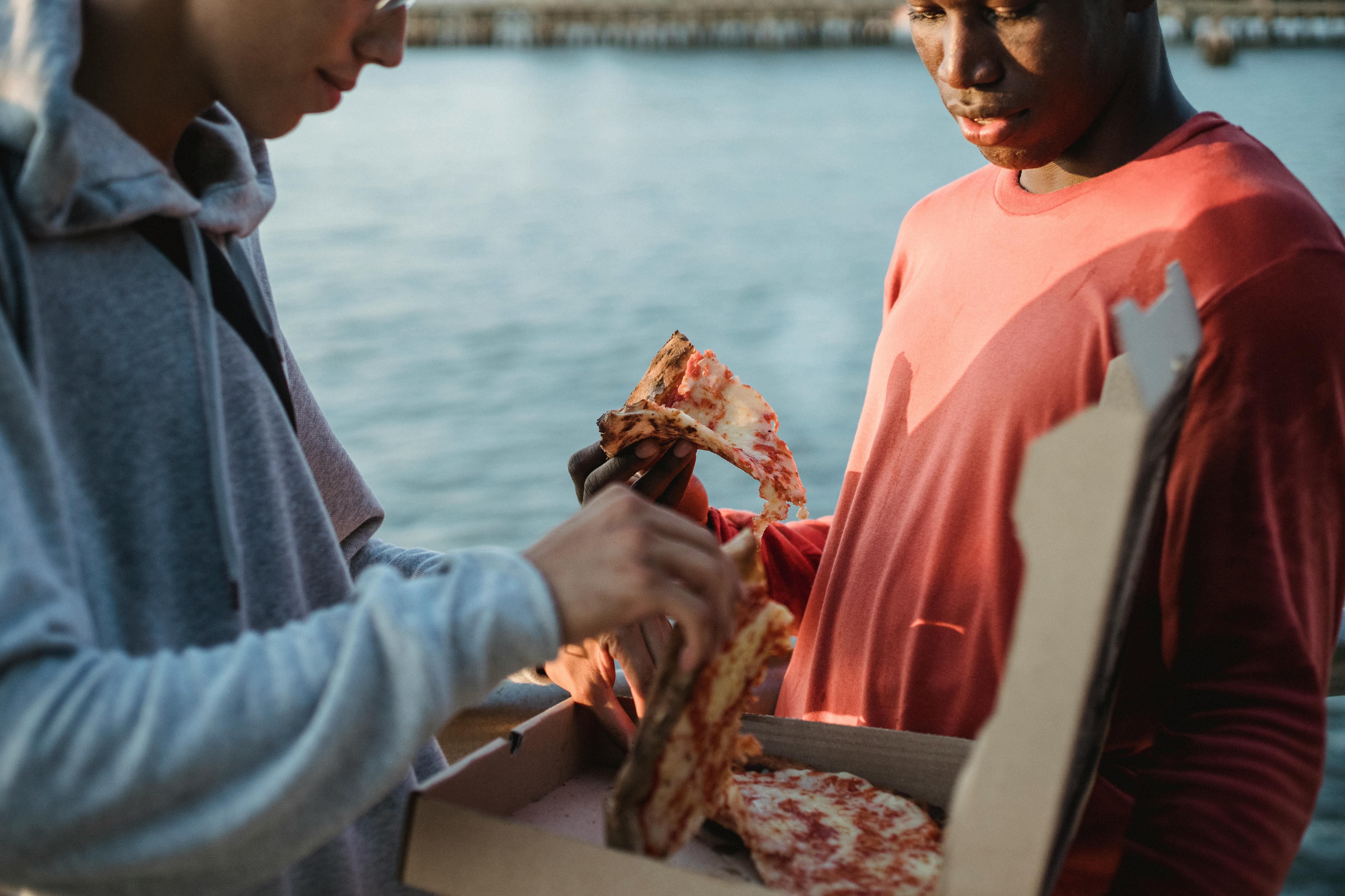 crop multiethnic men sharing yummy pizza on promenade